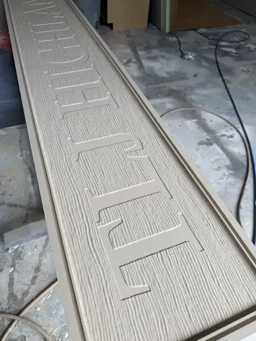 Close view of raised lettering and routed woodgrain on a long sign panel before finishing